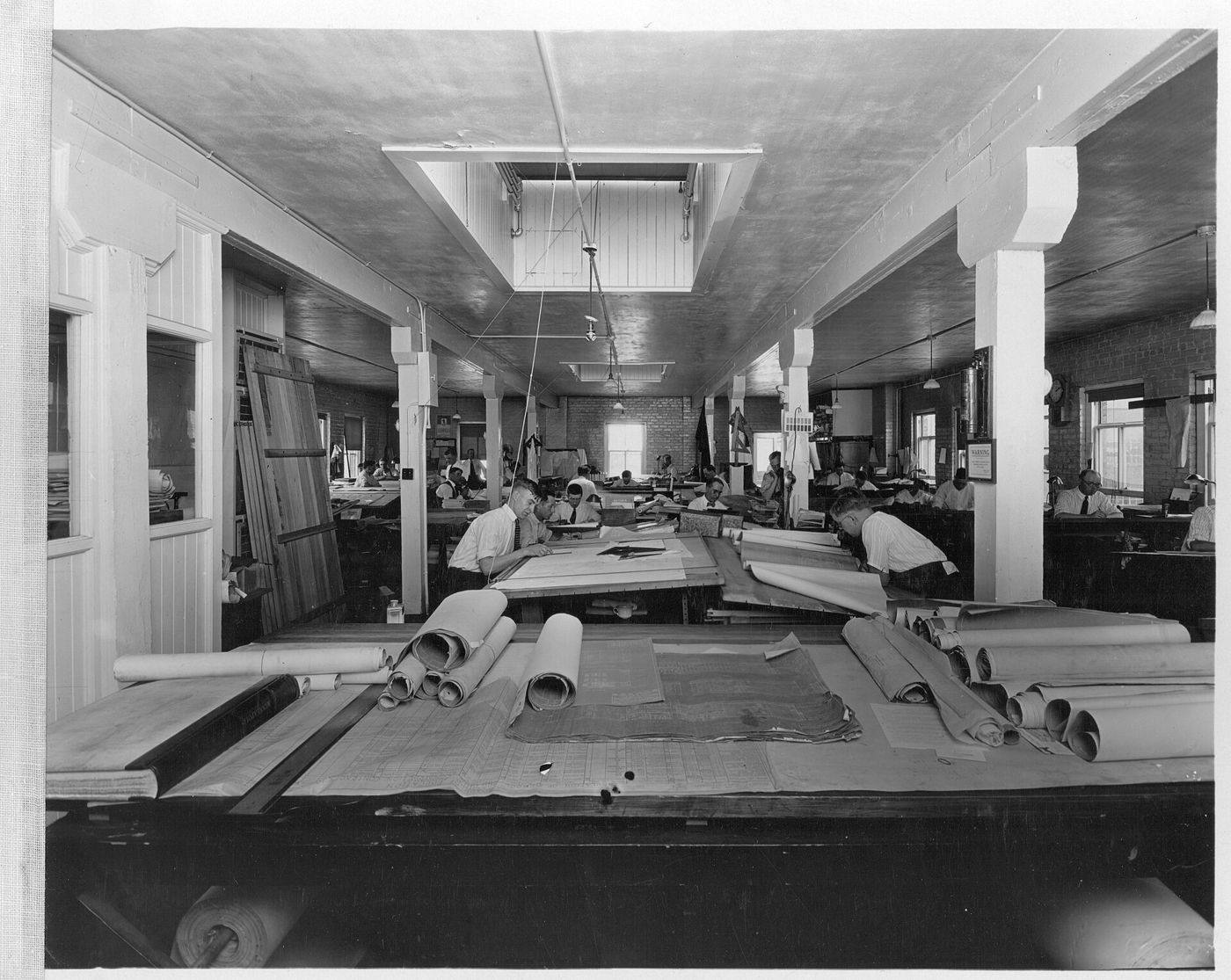 A drafting room in 1923, with draughtsmen bent over tables covered in plans